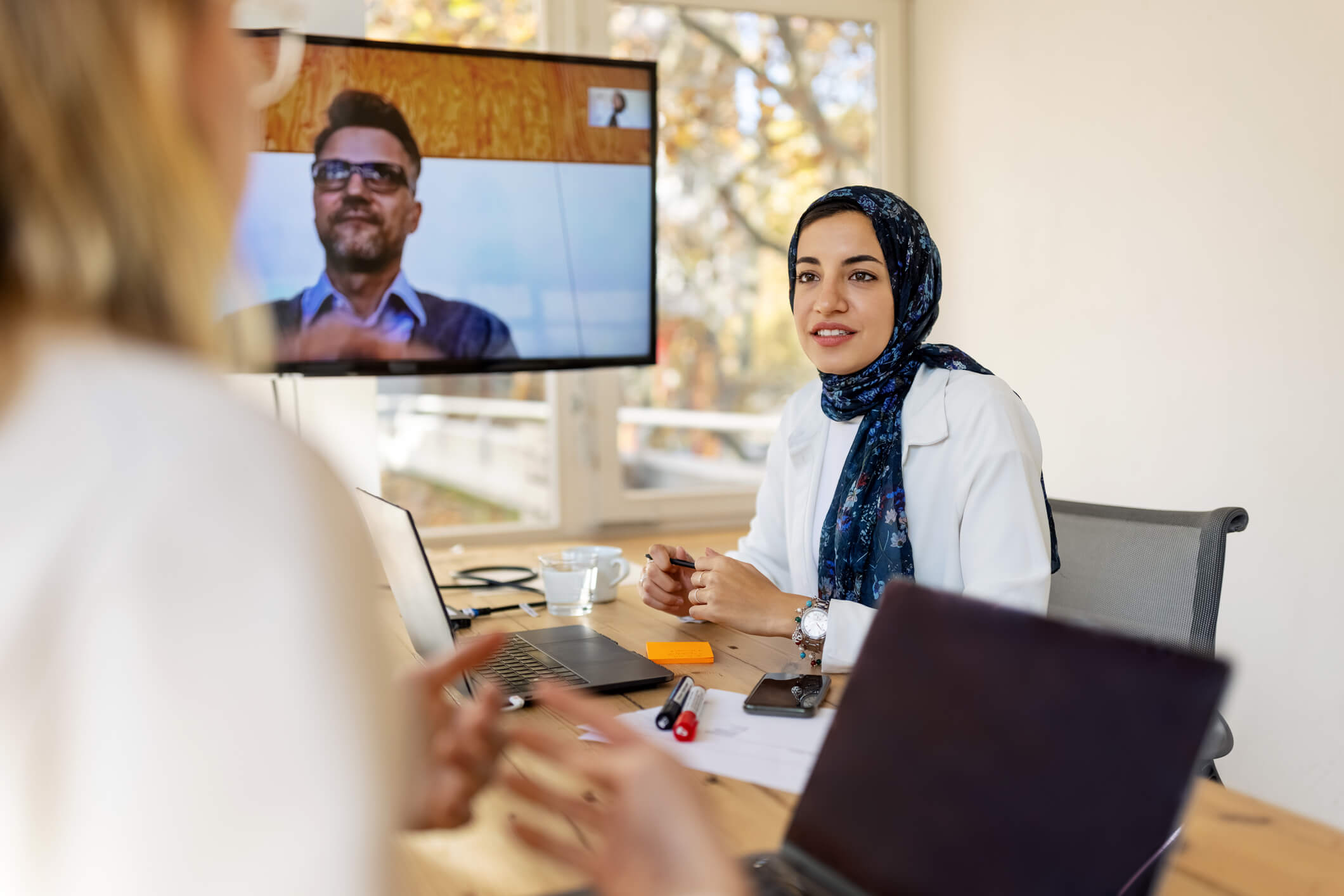 Business team having meeting at small office with colleague connecting on a video conference. Startup business professionals making strategies sitting in board room with a colleague on video call.